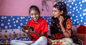 Mother with daughter sitting on bed sharing mobile phone screen